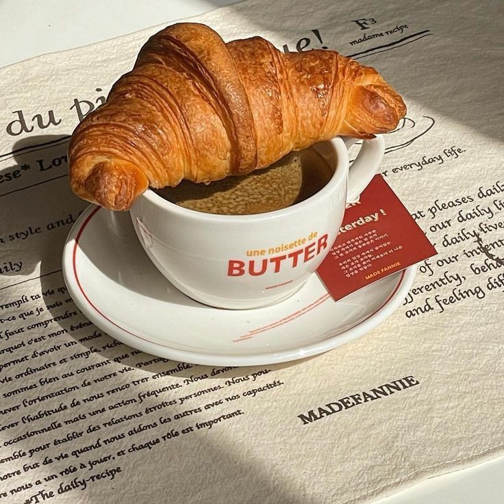 a croissant sitting in a cup on top of a saucer next to a piece of paper