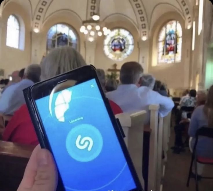 a person holding up a cell phone in front of a church with stained glass windows