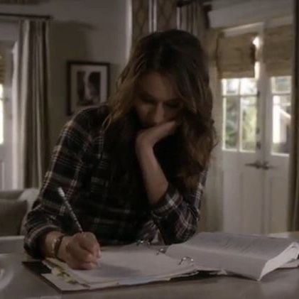 a woman sitting at a table writing on a book with a pen and paper in front of her