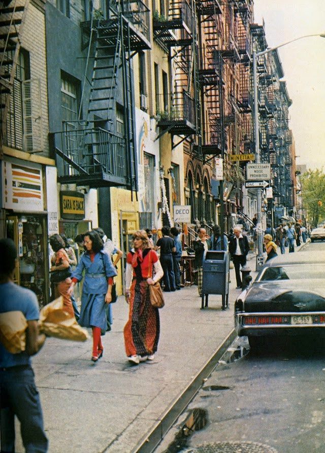 an old photo of people walking on the sidewalk in front of buildings and cars driving down the street