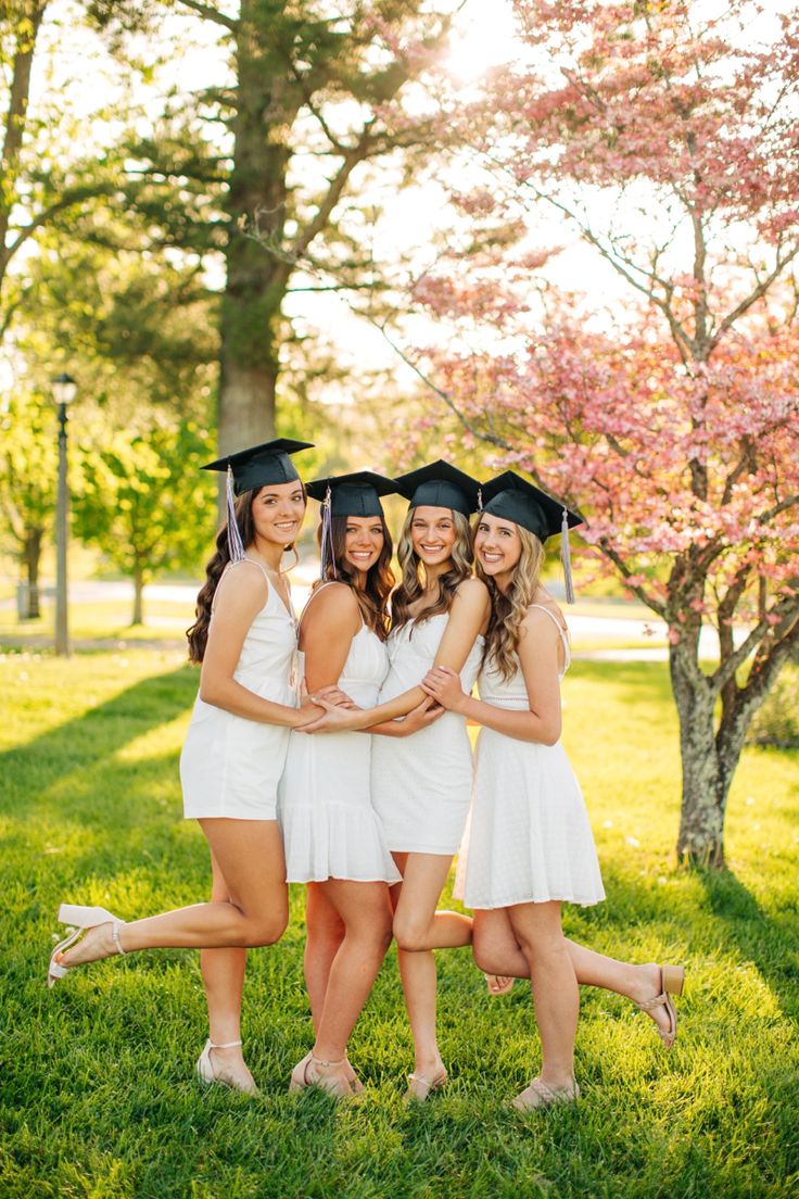 four young women in graduation gowns posing for a photo with their arms around each other