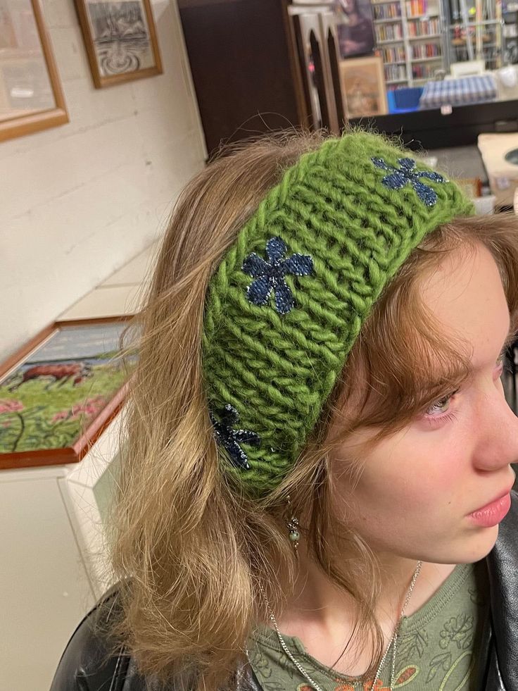 a girl wearing a green knitted headband with blue flowers on the front and side