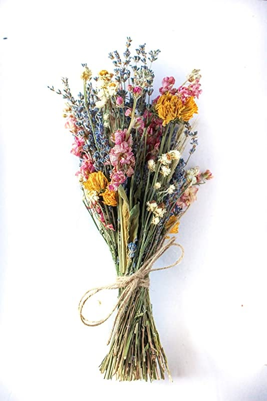 a bunch of dried flowers tied up to a white wall with a brown ribbon on it