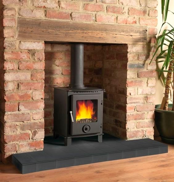 a wood burning stove sitting on top of a wooden floor next to a brick wall