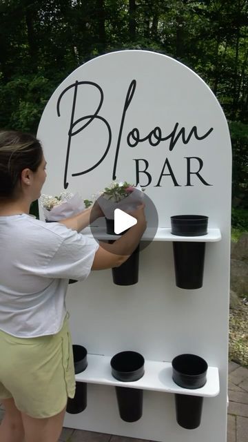 a woman placing flowers on a bloom bar sign with cups in front of the sign