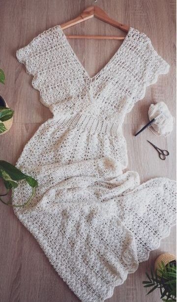 a white knitted dress sitting on top of a wooden floor next to a plant