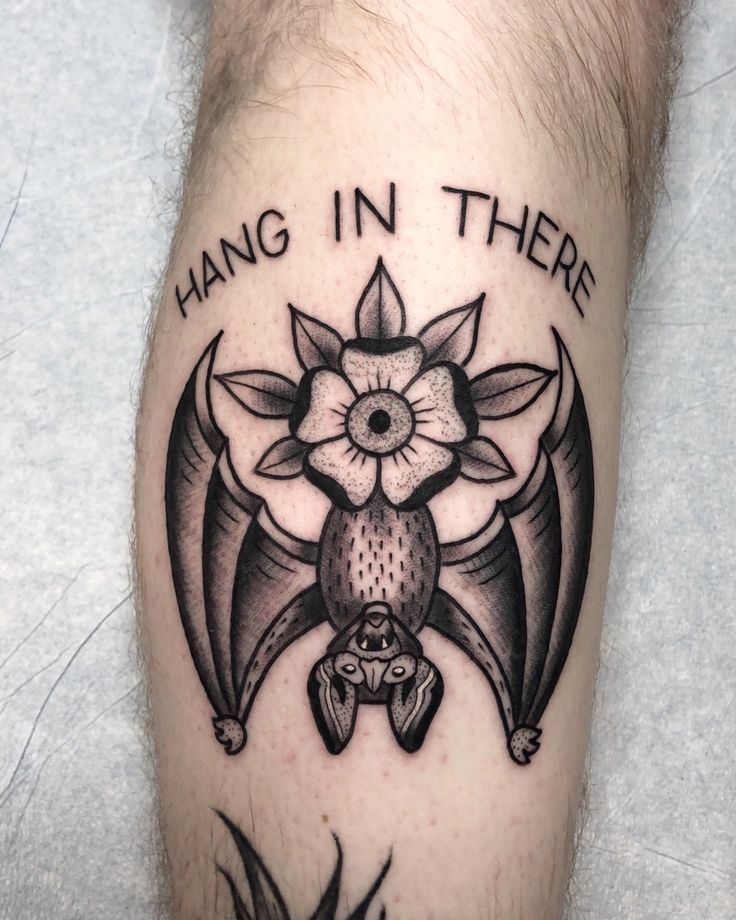 a tattoo on the leg of a man with words hang in there and an image of a bat