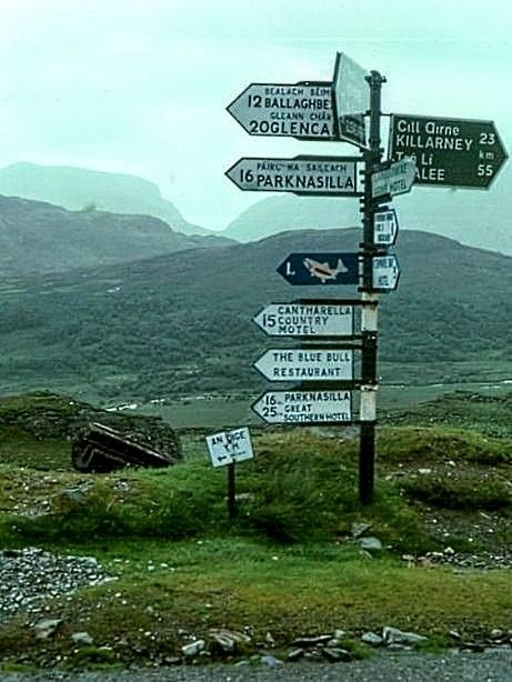 there are many signs on the pole in front of some hills and grass with mountains in the background