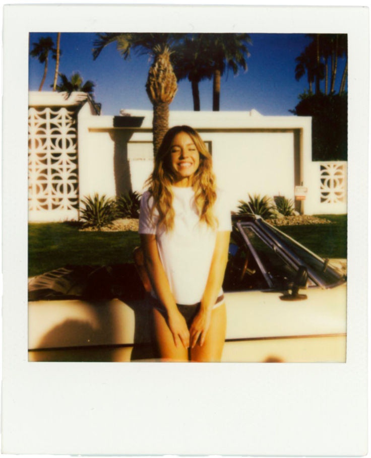 a woman posing for a photo in front of a white house with palm trees behind her