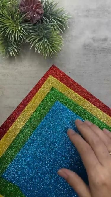 a hand is touching the top of a rainbow rug next to a potted plant