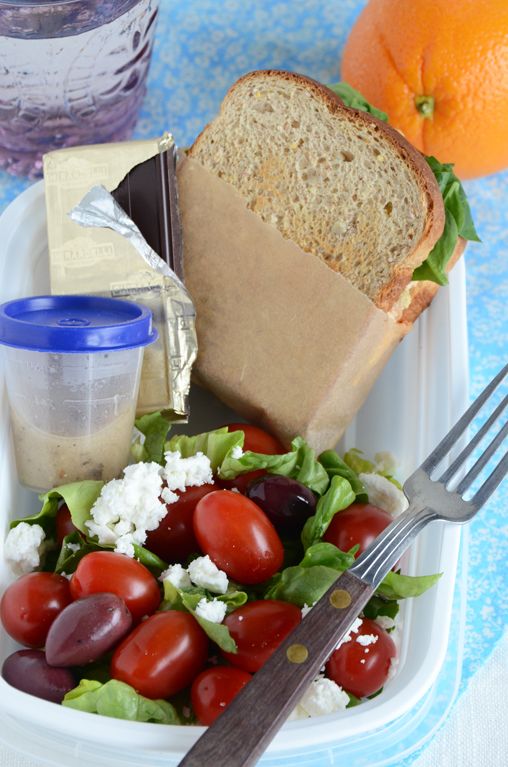 a sandwich and salad in a plastic container on a blue tablecloth with oranges