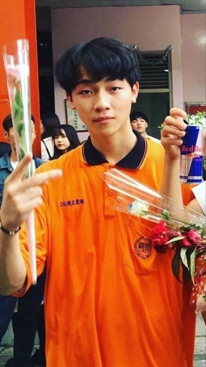 a young man is holding flowers and an empty tube in his hand while standing outside