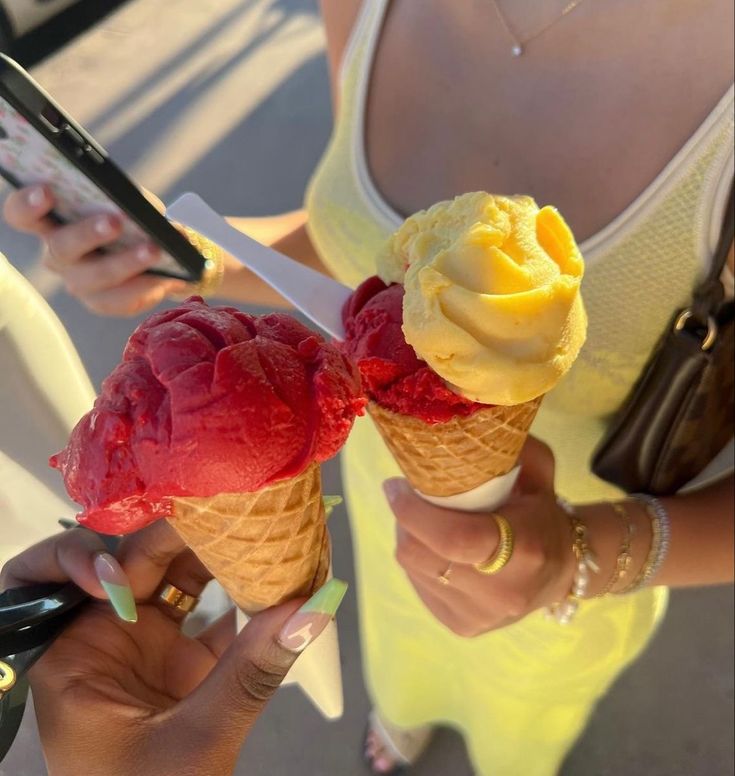 two scoops of ice cream are being held up by women in yellow dresses and one is holding a cell phone