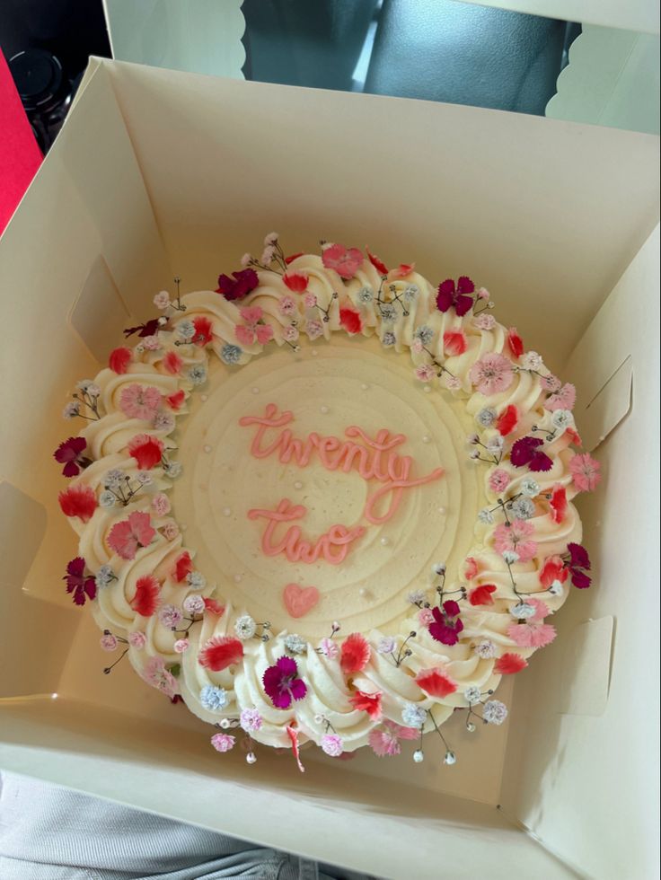 a white cake in a box with pink and red flowers on it's side