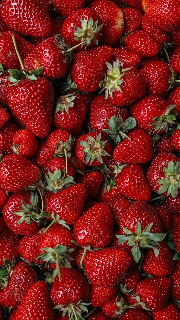 a large pile of red strawberries with green leaves