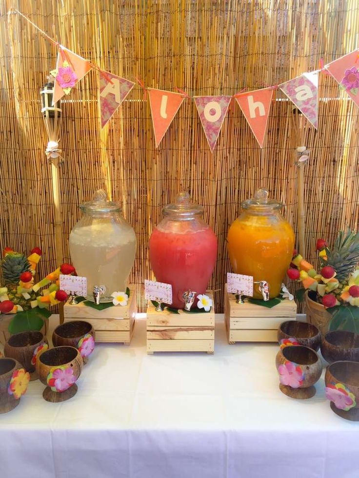 a table topped with vases filled with fruit and drinks next to a sign that says tiki bar - coconut, guava & mango juice