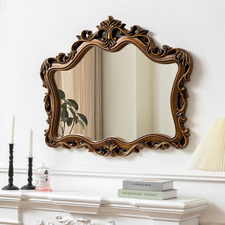 a mirror sitting on top of a white mantle next to a lamp and a book