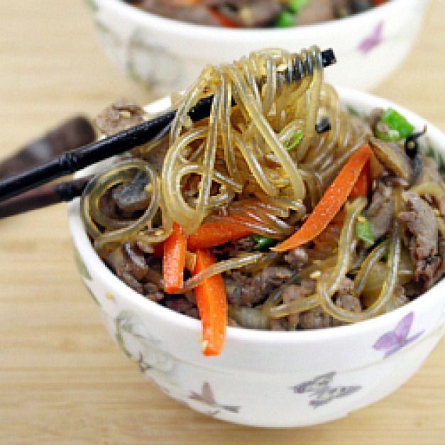 two bowls filled with noodles and vegetables on top of a wooden table next to chopsticks