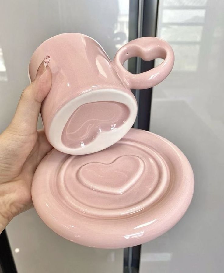 a hand holding a pink coffee mug with a heart shaped handle