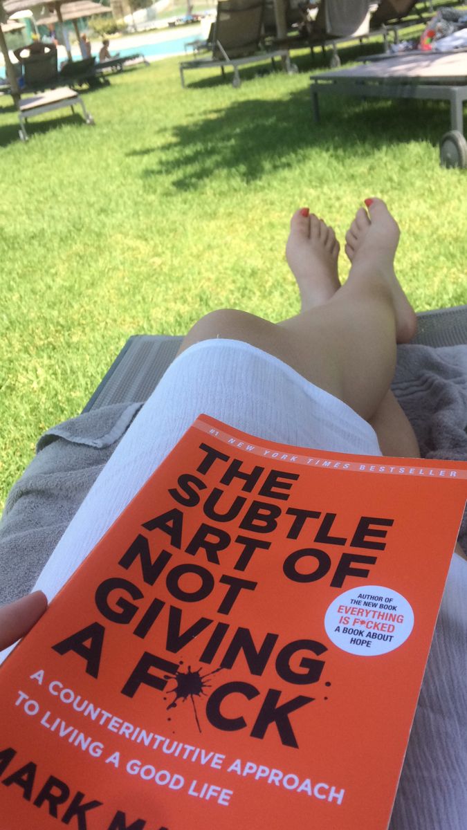 a person laying in the grass with a book on it's lap reading the subtle art of not giving a f k