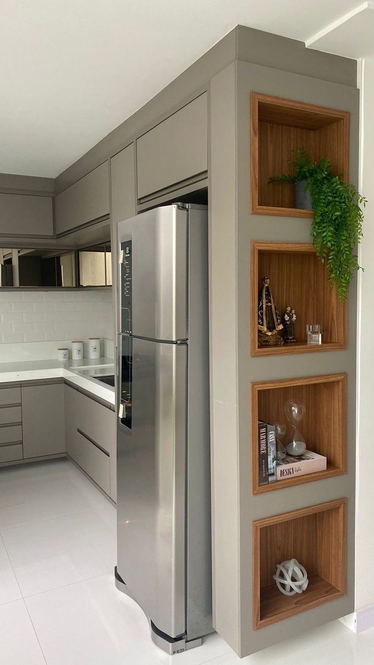 a stainless steel refrigerator in a kitchen with wooden shelves on the wall and white tile flooring