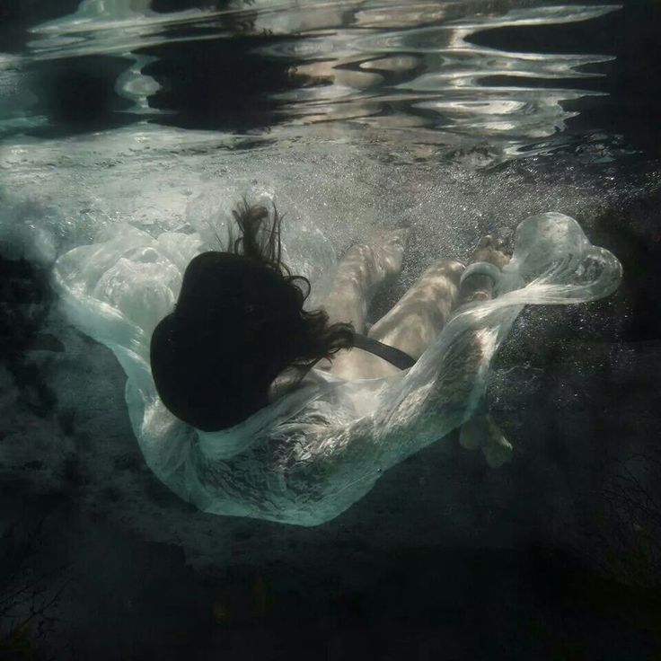 a woman floating in the water on top of a white sheet with her hair blowing back