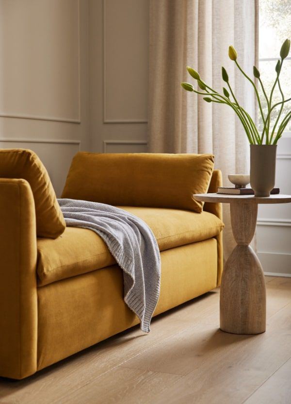 a yellow couch with a blanket on it next to a table and potted plant