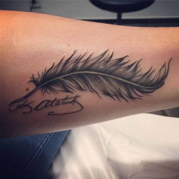 a black and white photo of a feather with the word tattoo on it's arm