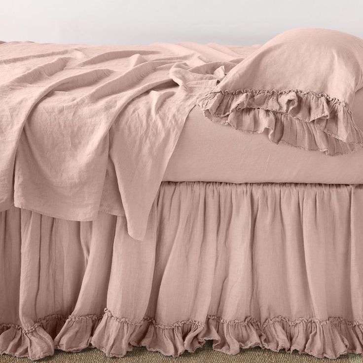 a pink bed with ruffled bedspread and pillowcases on the floor