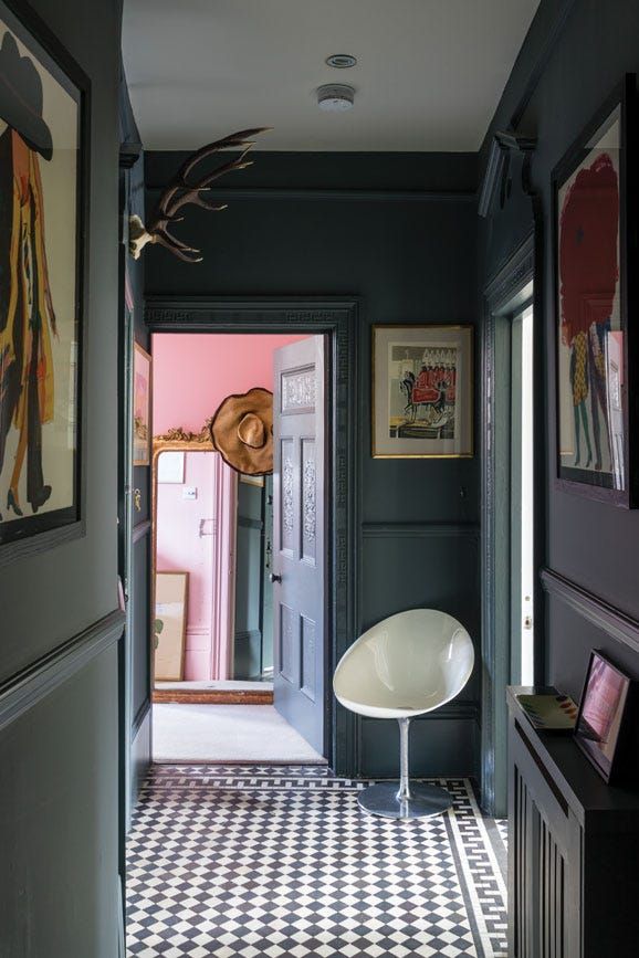 a hallway with black walls and white checkered flooring, framed pictures on the wall