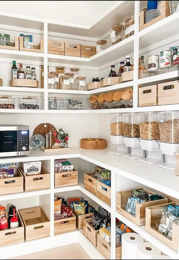 an organized pantry with white shelves and wooden bins