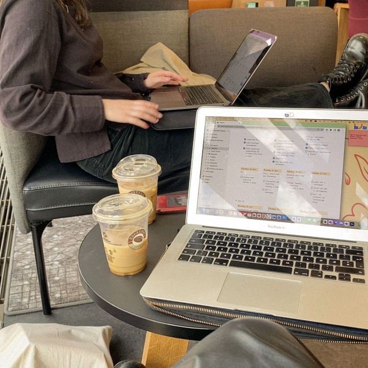 a woman sitting on a couch using a laptop computer next to a cup of coffee