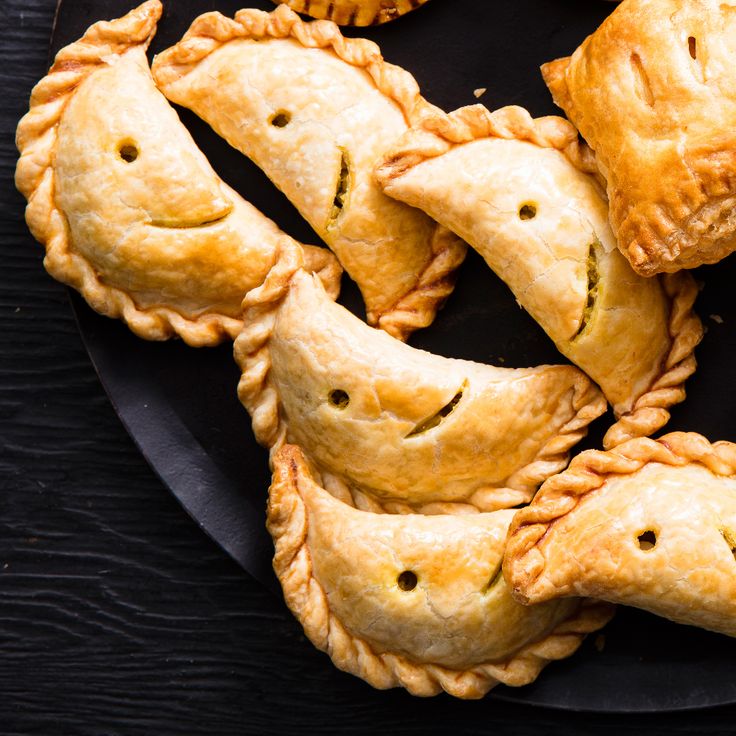 several pastries on a black plate with faces drawn on the top and one has been cut in half