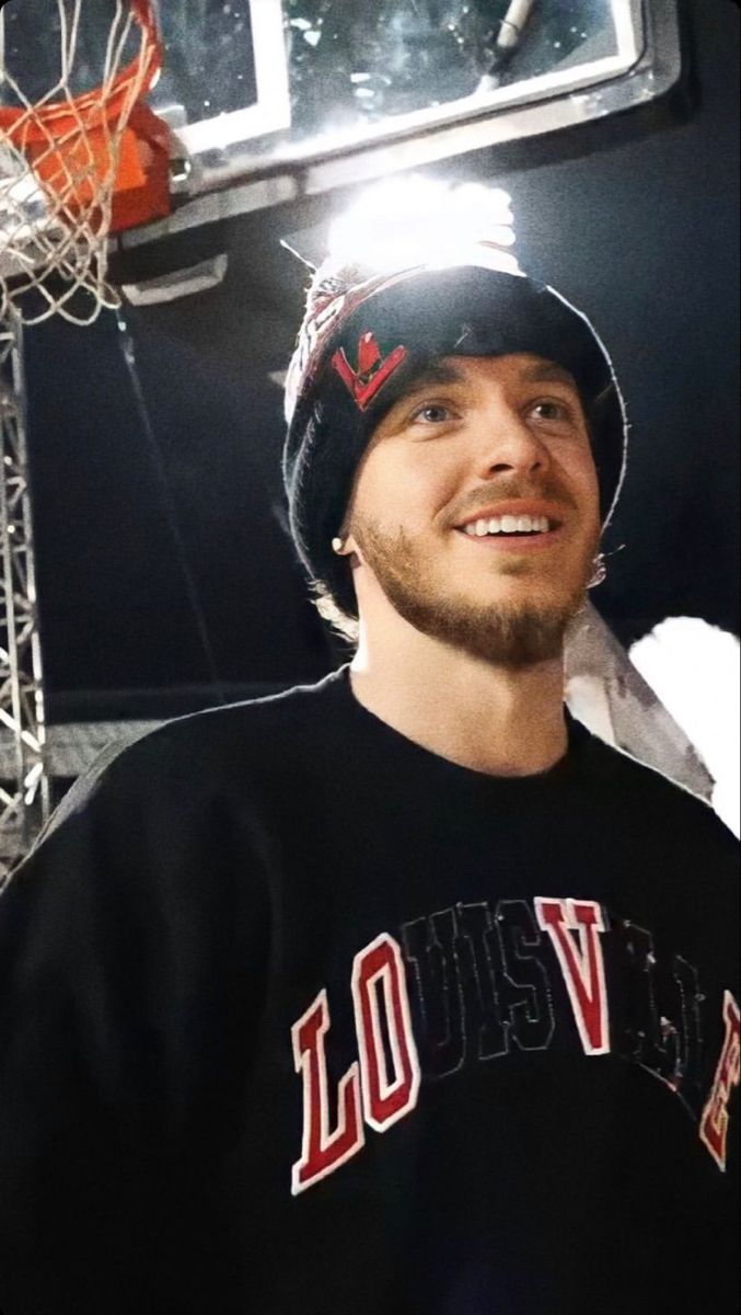 a man standing in front of a basketball hoop wearing a black sweater and beanie