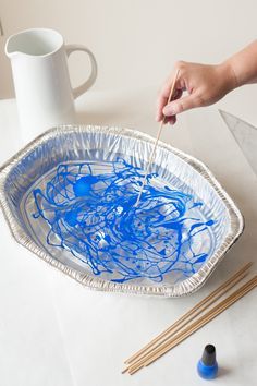 someone is painting on a paper plate with blue paint and chopsticks in front of them