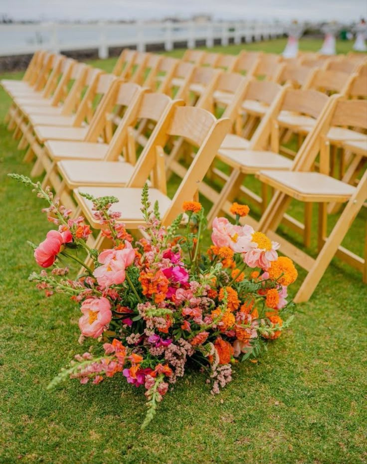 rows of wooden chairs with flowers on the grass in front of them at an outdoor ceremony