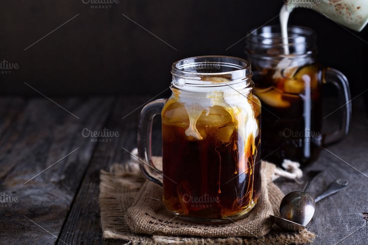 iced coffee being poured into a mason jar with spoons on a wooden table top