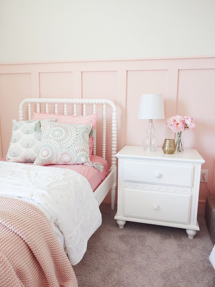 a white bed sitting next to a pink wall with flowers on top of it and two nightstands