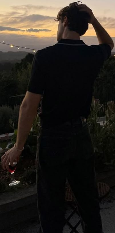 a man standing on top of a roof next to a lush green field at sunset