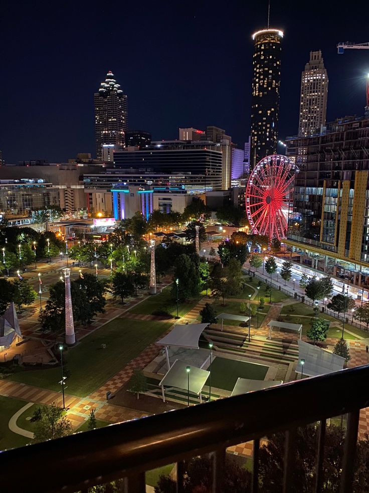 the city skyline is lit up at night with ferris wheel in foreground and lights on buildings