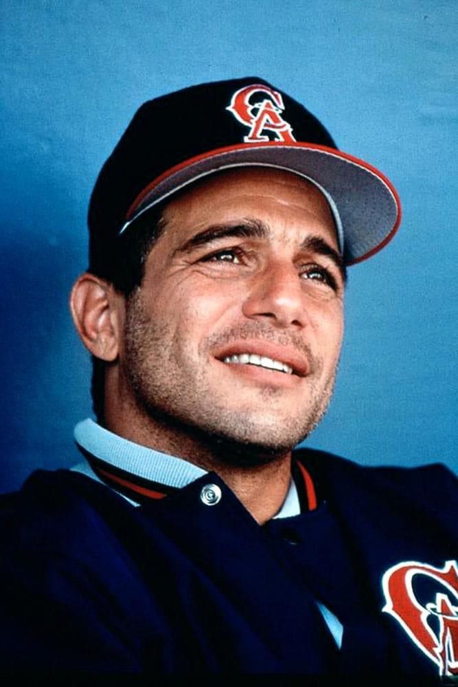 a professional baseball player poses for a photo in his uniform and cap, smiling at the camera