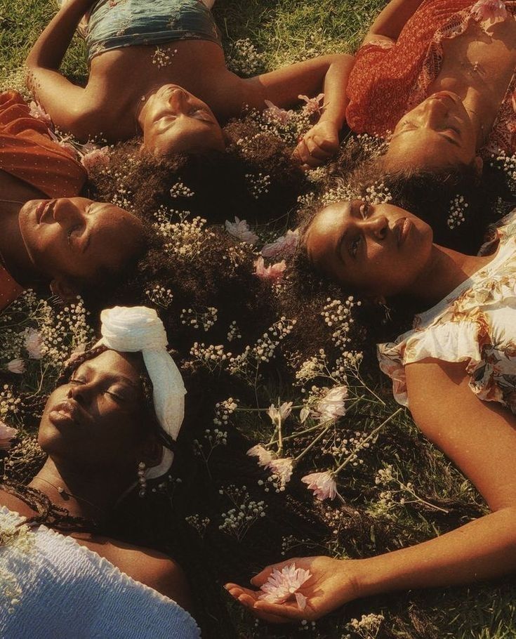 four women laying on the grass with flowers in their hair and wearing headbands