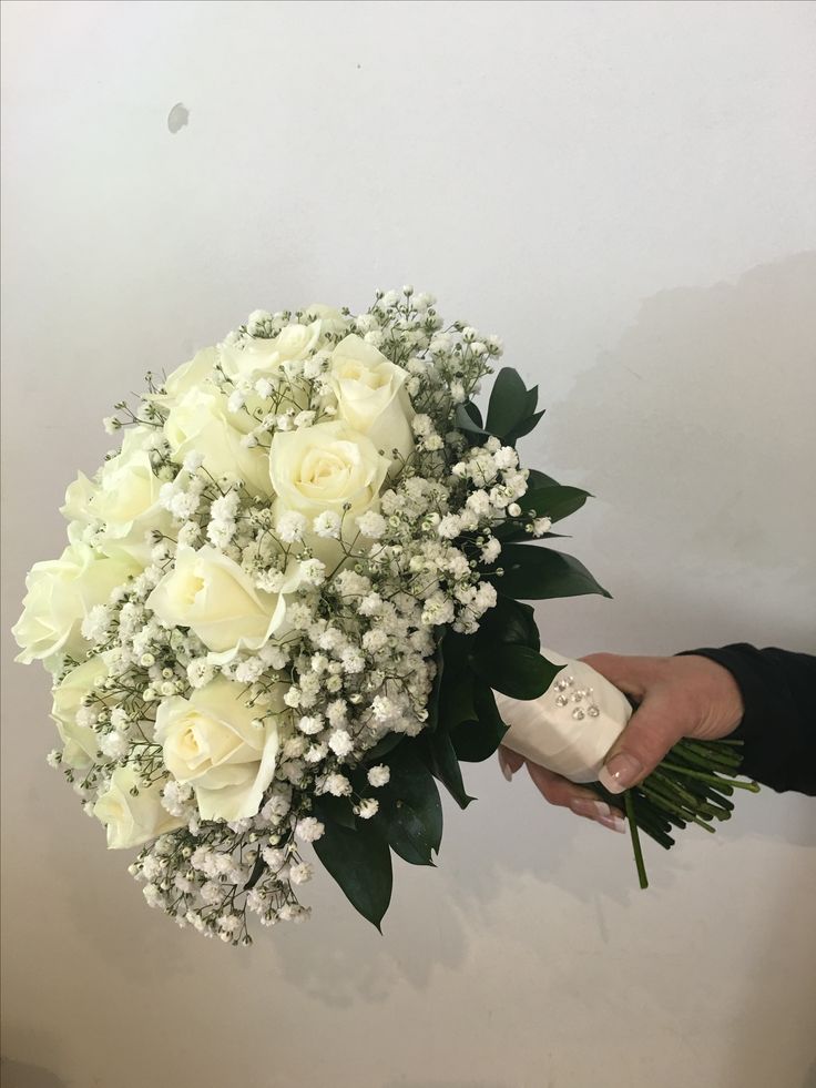 a bouquet of white flowers being held by a person's hand in front of a wall