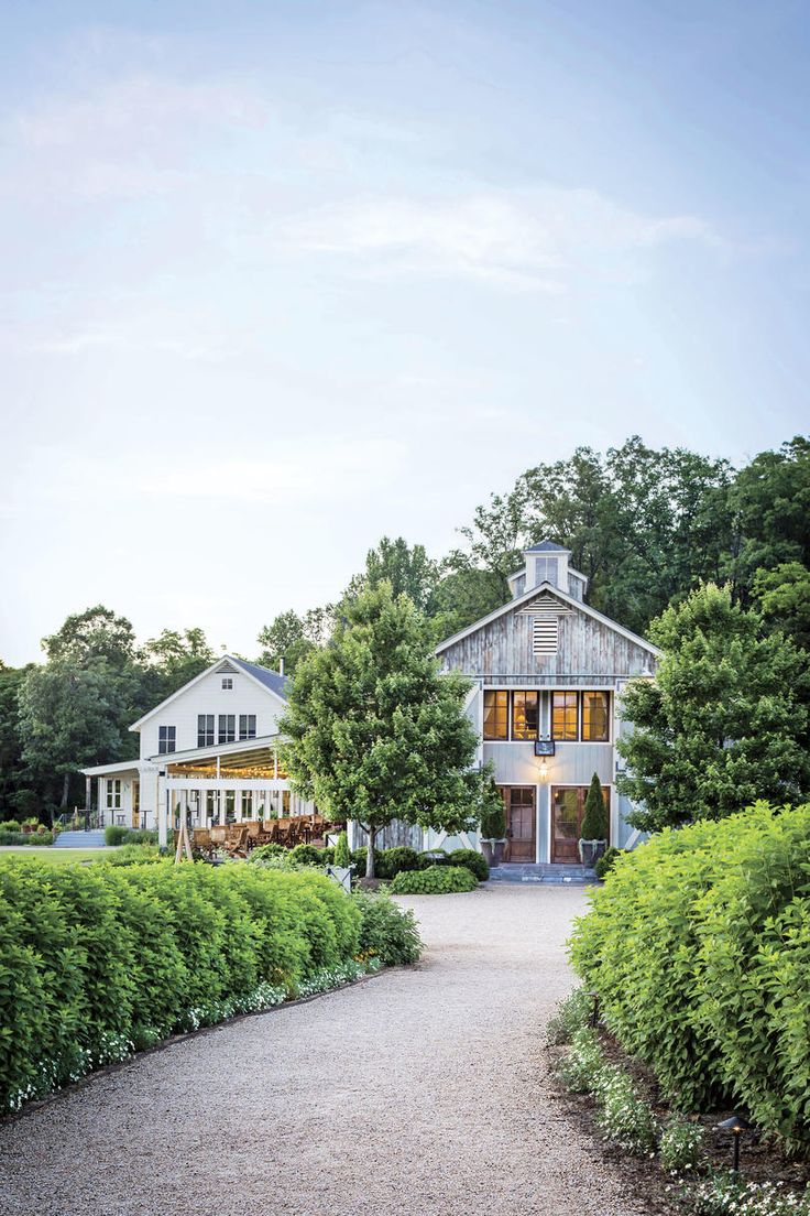 a white house surrounded by lush green trees and shrubbery with a pathway leading to the front door