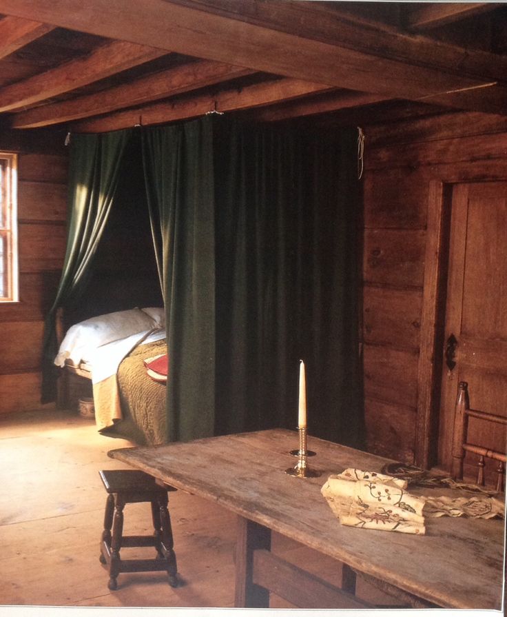 an old table and chair in a room with wooden walls, green drapes on the windows