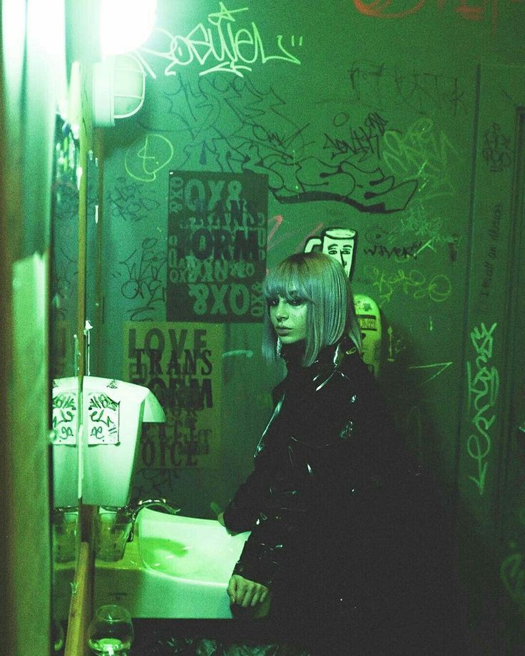 a woman standing in front of a urinal with graffiti on the wall behind her