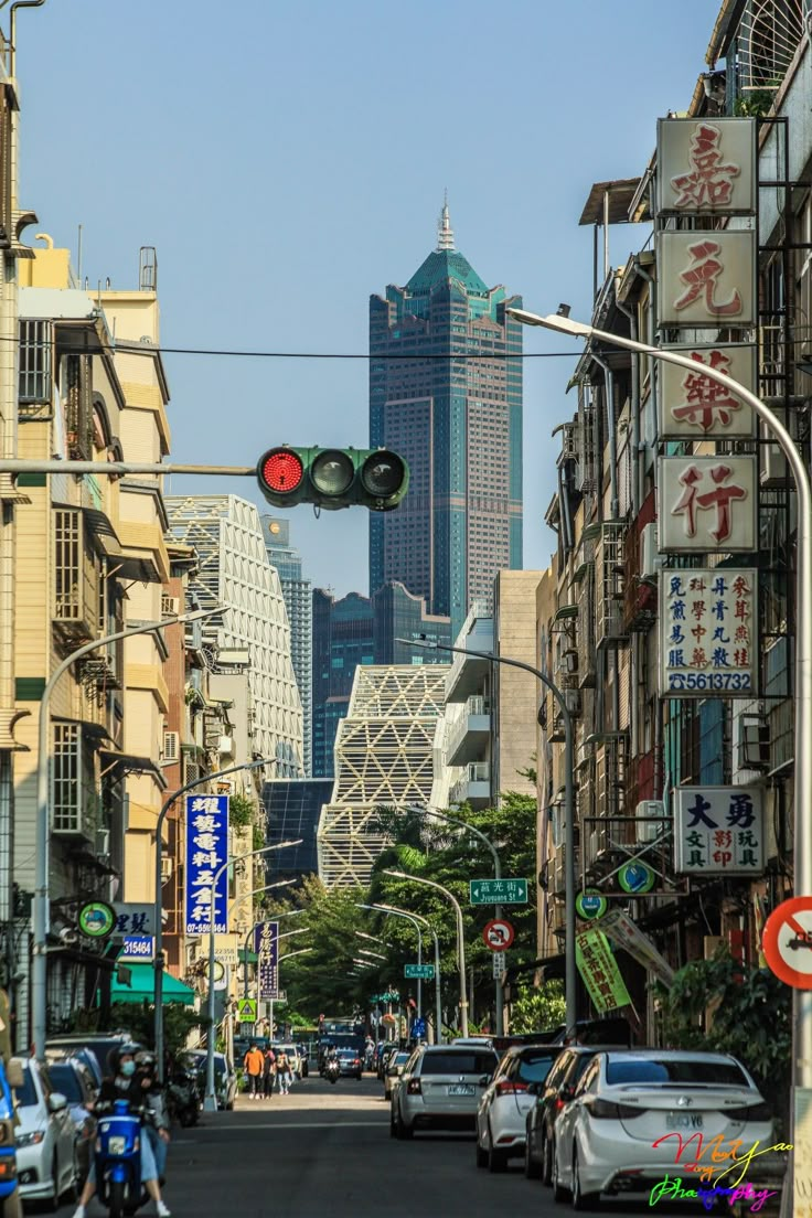 a city street with cars and motorcycles on the side walk, traffic lights in front of tall buildings