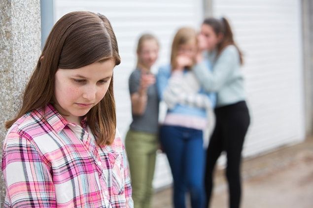 a group of girls standing next to each other in front of a building with one girl looking down at her cell phone