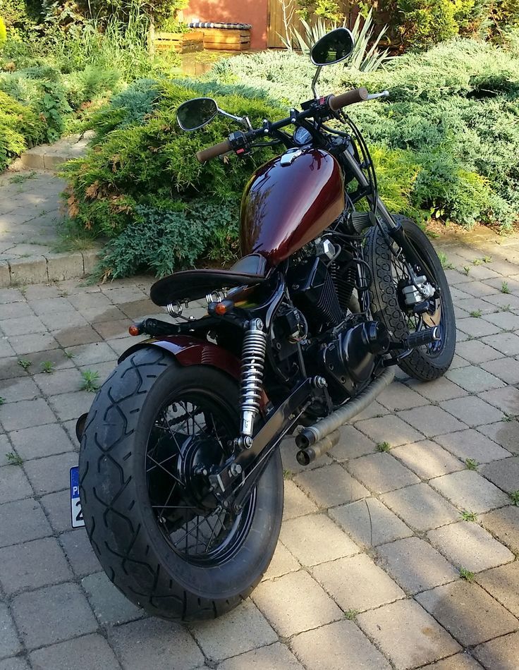 a red motorcycle parked on top of a brick road next to bushes and trees in the background