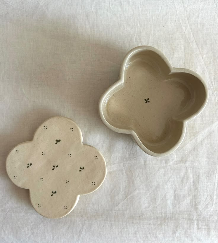 two ceramic dishes sitting on top of a white cloth covered tablecloth, one has a cloud shaped dish and the other has paw prints